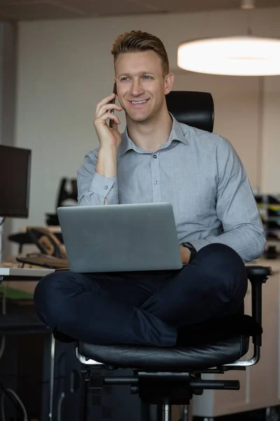 Executivo falando por telefone ao usar laptop — Fotografia de Stock