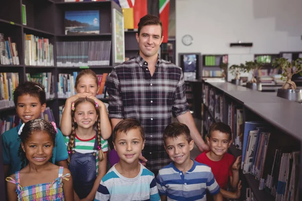 Maestro y escolares de pie juntos en la biblioteca — Foto de Stock