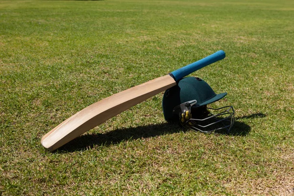 Крикетна кажана і шолом на полі — стокове фото