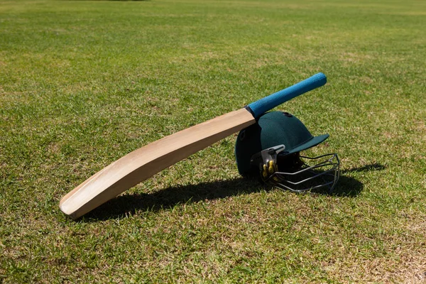 Cricket bat and helmet on field — Stock Photo, Image