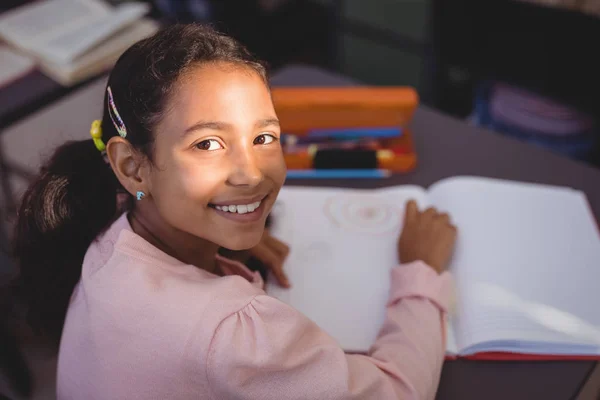 Glimlachend schoolmeisje zijn huiswerk in bibliotheek — Stockfoto