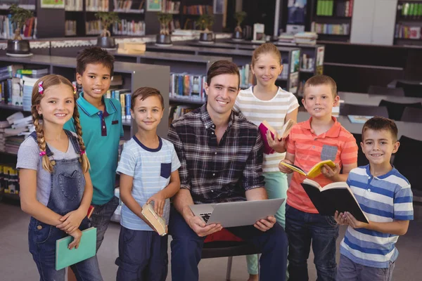 Maestro y los escolares que utilizan el ordenador portátil en la biblioteca — Foto de Stock