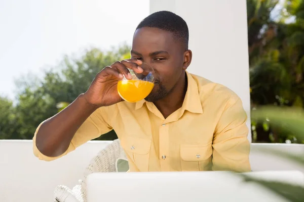 Mannen dricker apelsinjuice medan du tittar på laptop — Stockfoto