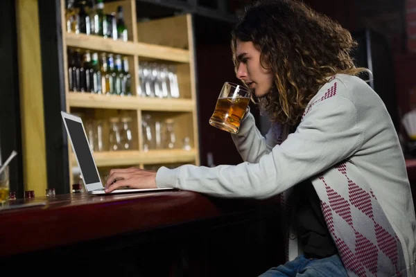 Ο άνθρωπος που έχει μπύρα ενώ χρησιμοποιείτε φορητό υπολογιστή στο γκισέ — Φωτογραφία Αρχείου