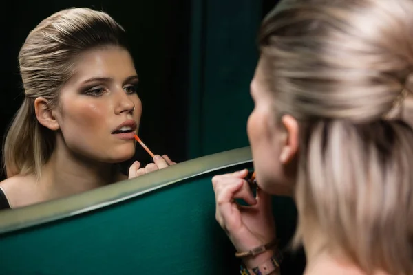 Mujer aplicando brillo de labios mientras mira el espejo —  Fotos de Stock