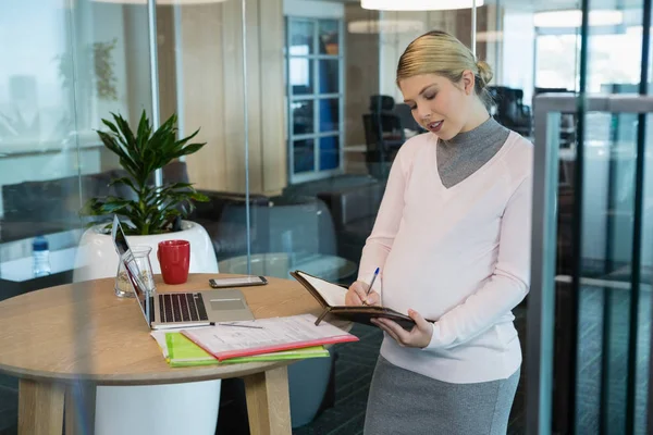 Femme d'affaires enceinte écrivant sur organisateur — Photo