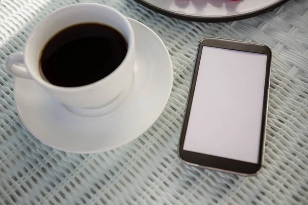 Taza de café por teléfono en la mesa en la cafetería —  Fotos de Stock