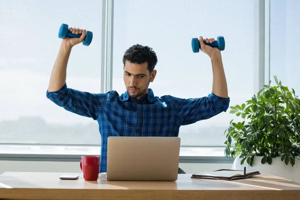 Executive exercising with dumbbells while working — Stock Photo, Image