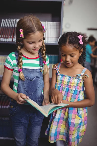 Colegialas atentas leyendo libro en la biblioteca — Foto de Stock