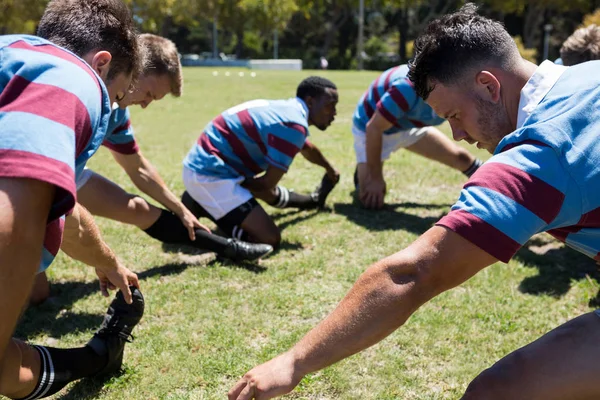 Rugby players touching toes at field — Stock Photo, Image