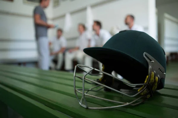 Capacete de críquete na mesa contra a equipe — Fotografia de Stock