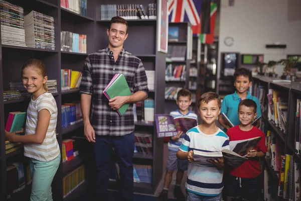 Δάσκαλος και φορητούς schoolkids στέκεται με βιβλία στη βιβλιοθήκη — Φωτογραφία Αρχείου