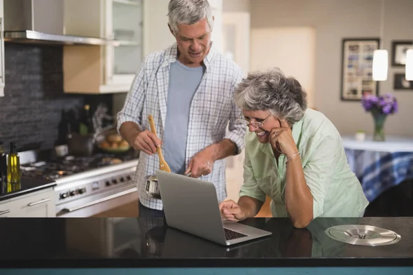 Üst düzey kadın kocasıyla mutfakta birlikte dizüstü bilgisayar kullanarak — Stok fotoğraf