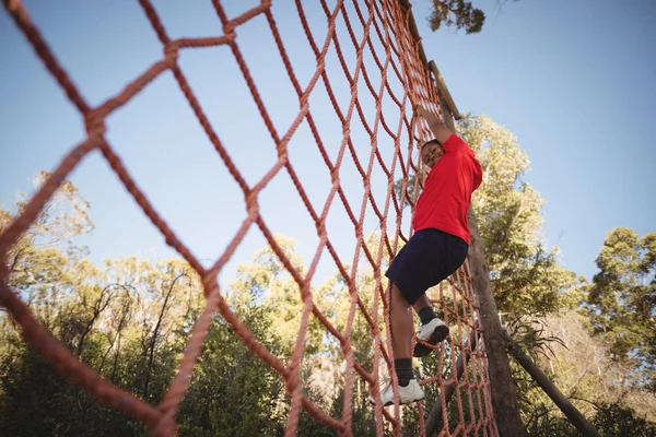 Menino escalando uma rede durante o curso de obstáculo — Fotografia de Stock