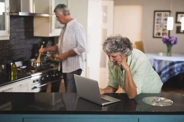 Fru med hjälp av laptop och make matlagning — Stockfoto