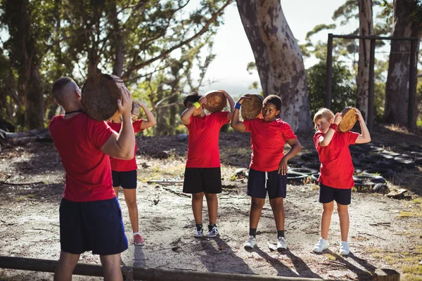Entrenador y niños llevando troncos de madera —  Fotos de Stock