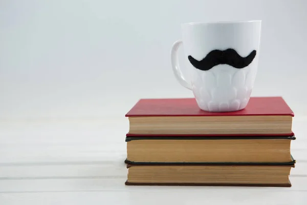 Tasse avec moustache sur les livres — Photo