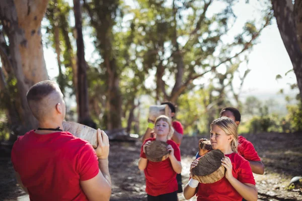 Entrenador y niños llevando troncos de madera — Foto de Stock