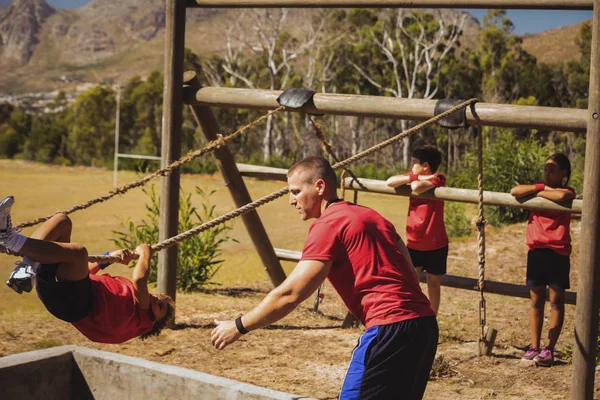 Entrenador asistiendo al chico en el campo de entrenamiento —  Fotos de Stock