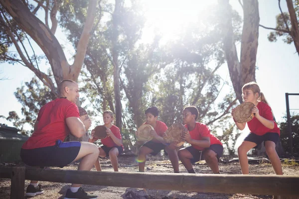 Trainer and kids carrying wooden logs — Stock Photo, Image