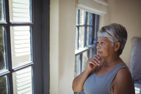 Doordachte senior vrouw op zoek door raam — Stockfoto