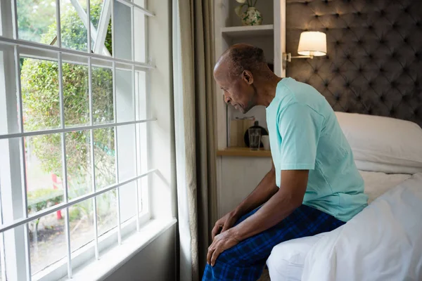 Thoughtful senior man sitting on bed by window — Stock Photo, Image