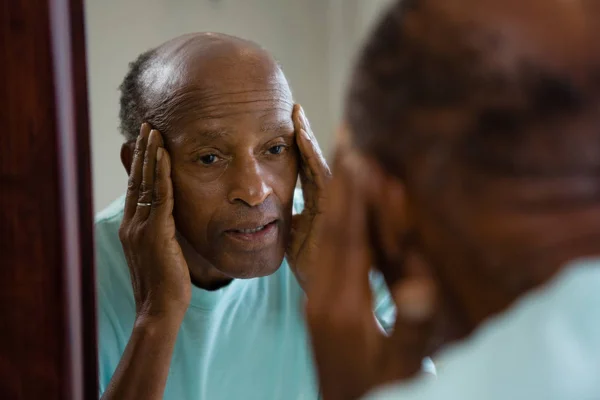 Обеспокоенный пожилой человек, размышляющий над зеркалом — стоковое фото