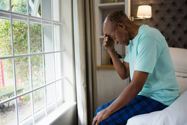 Triest senior man zittend op bed door raam thuis — Stockfoto