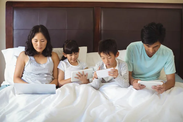 Familj med hjälp av elektroniska apparater i sovrum — Stockfoto