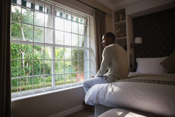 Pencere yatak odasında yatağın üzerinde oturan adam — Stok fotoğraf