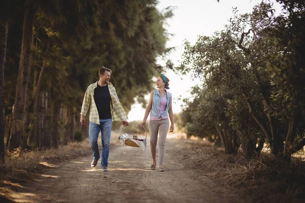 Couple carrying basket while walking on dirt road — Stock Photo, Image