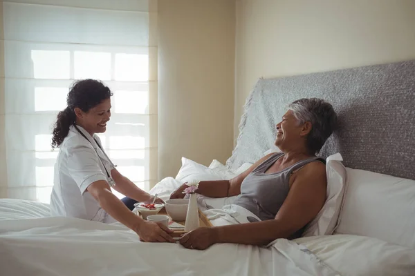 Medico che serve la colazione alla donna anziana sul letto — Foto Stock