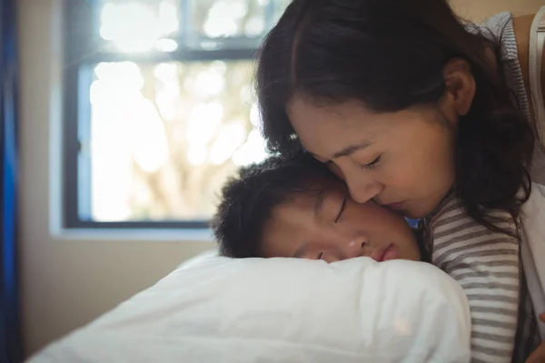 Madre baciare figlio su guance in camera da letto — Foto Stock