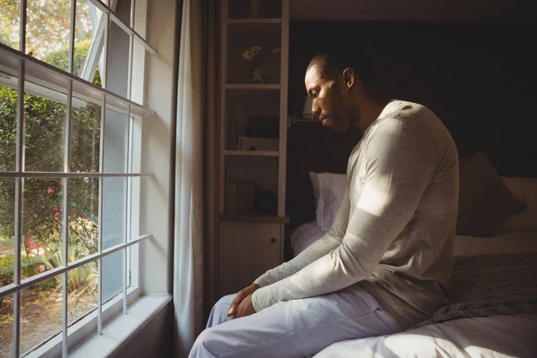 Sad man sitting on bed by window — Stock Photo, Image