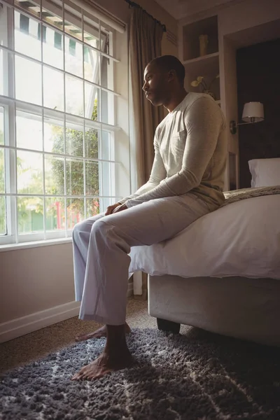 Homme réfléchi assis sur le lit par la fenêtre — Photo