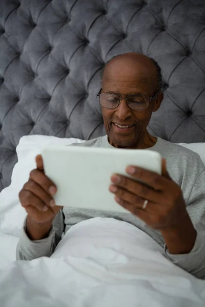 Homem idoso usando tablet enquanto descansa na cama — Fotografia de Stock