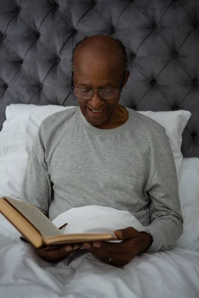 Senior homme lecture livre tandis que sur le lit — Photo