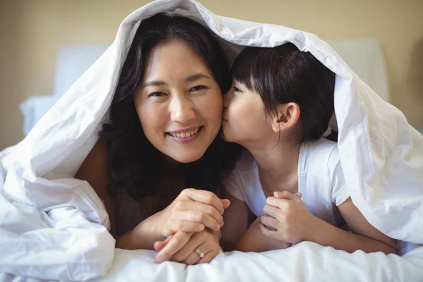 Дочь целует свою мать под одеялом — стоковое фото