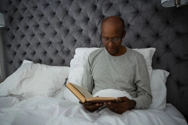 Senior homme lecture livre tandis que sur le lit — Photo