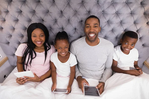 Retrato de la familia sonriente sosteniendo tabletas digitales en la cama —  Fotos de Stock