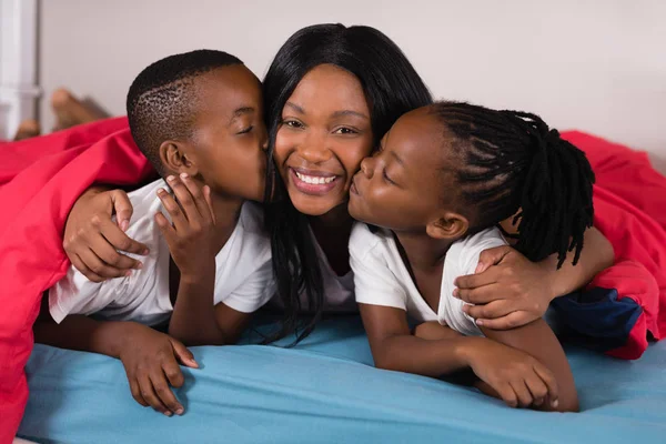 Siblings kissing their mother while lying on bed — Stock Photo, Image