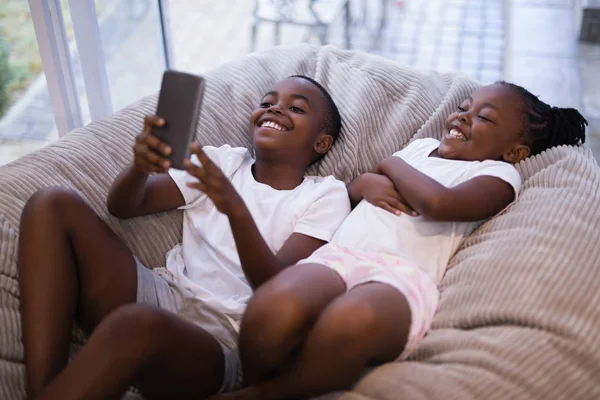 Hermanos usando el teléfono mientras están acostados en el sofá —  Fotos de Stock