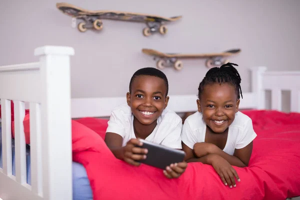 Frères et sœurs avec téléphone couché sur le lit à la maison — Photo