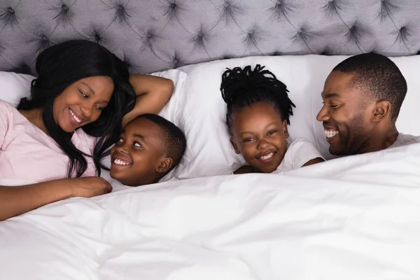 Девушка, лежащая со счастливой семьей на кровати — стоковое фото