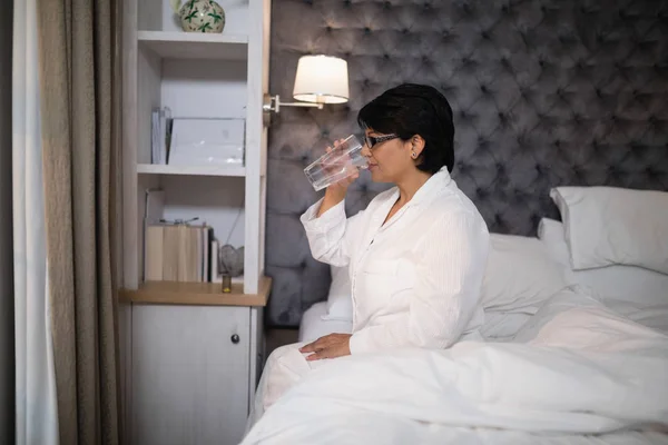Mujer beber agua mientras está sentado en la cama — Foto de Stock