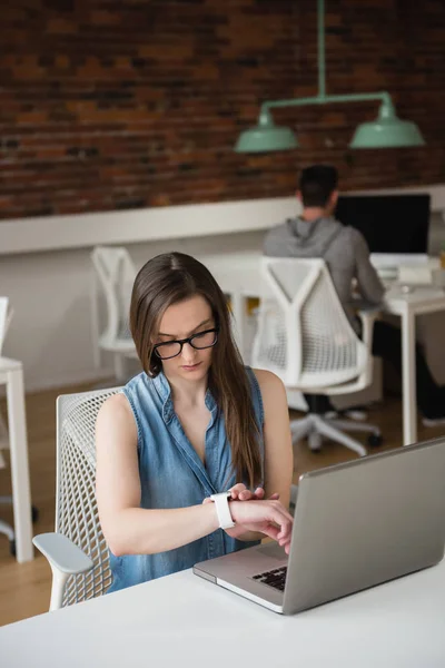 Female executive adjusting smart watch at desk — Stock Photo, Image