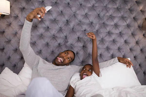 Travieso padre e hijo tomando selfie en la cama —  Fotos de Stock