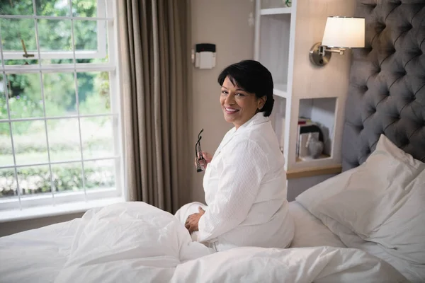 Woman sitting in illuminated bedroom — Stock Photo, Image