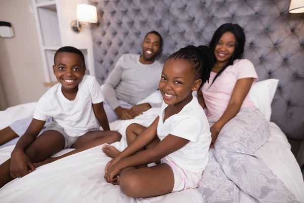 Smiling family sitting on bed — Stock Photo, Image