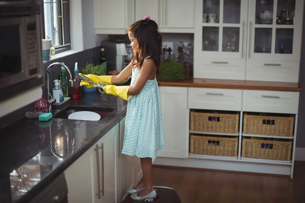 Cute little girl washing utensil in kitchen sink — Stock Photo, Image